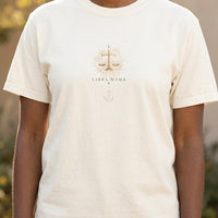 Close-up of ivory Libra Mama t-shirt showing gold scale design and moon stack detail on chest.