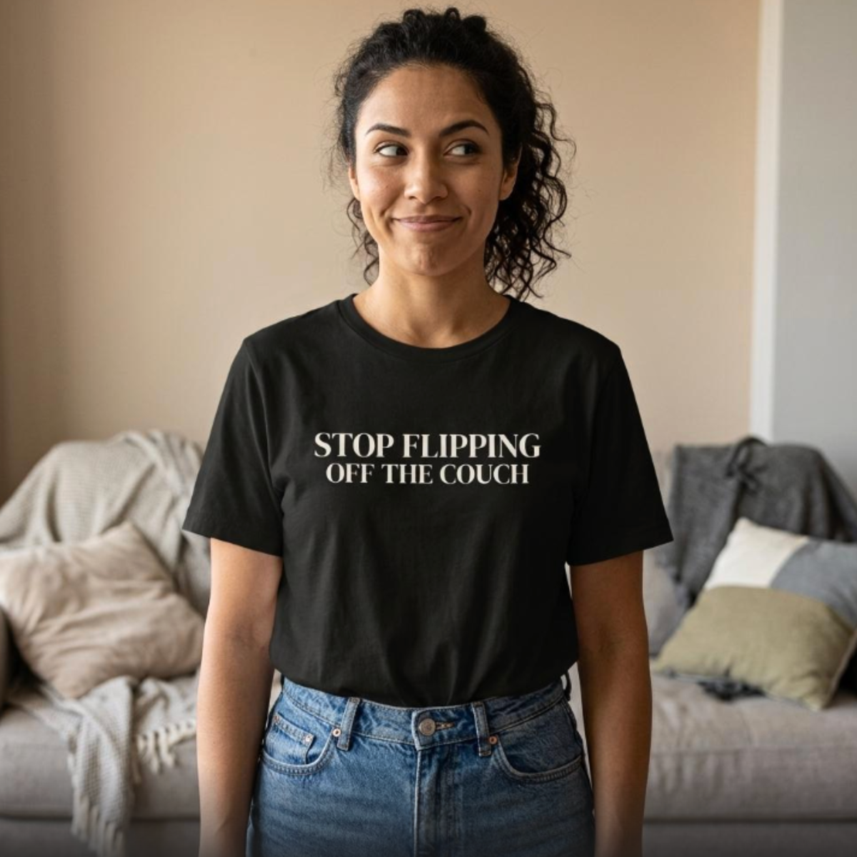 Woman wearing black “Stop Flipping Off the Couch” t-shirt standing in cozy home setting, relaxed everyday style
