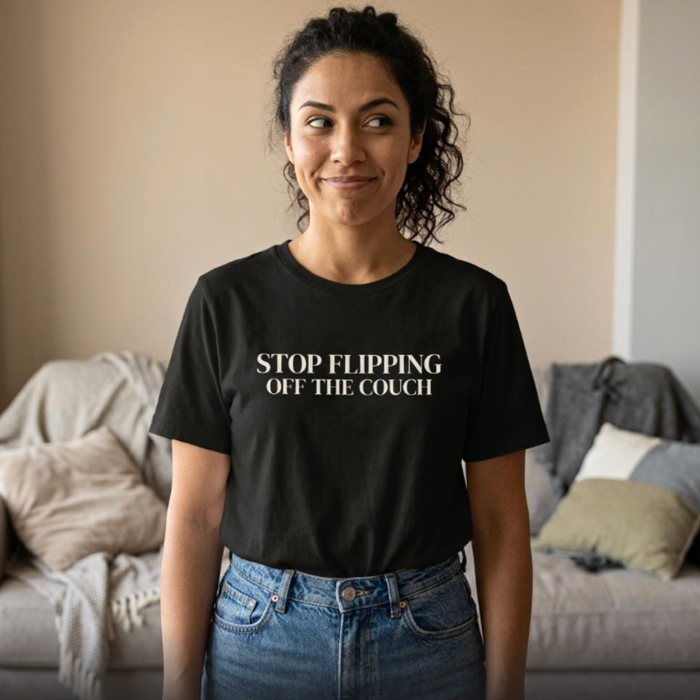 Woman wearing black “Stop Flipping Off the Couch” t-shirt standing in cozy home setting, relaxed everyday style