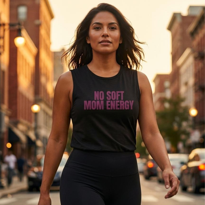 Woman walking in city wearing black “No Soft Mom Energy” muscle tank with plum lettering