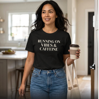 Woman wearing black “Running on Vibes & Caffeine” t-shirt indoors holding coffee, relaxed mom lifestyle outfit