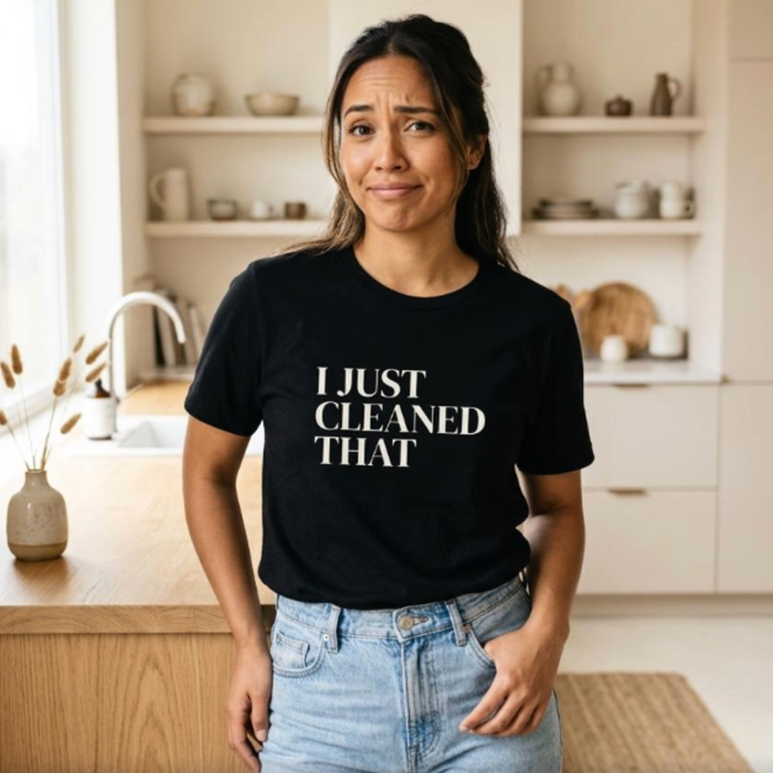 Black “I Just Cleaned That” graphic t-shirt on woman in kitchen, funny mom shirt with relatable expression