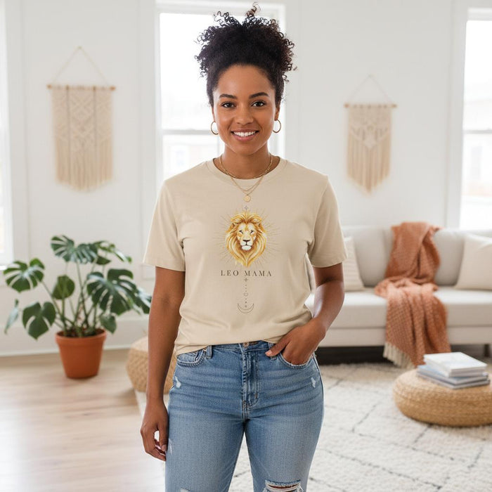 Woman of color wearing an ivory Leo Mama graphic t-shirt standing indoors in a bright neutral living room