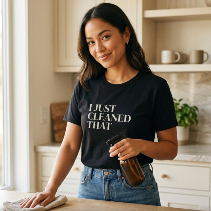 Woman wearing black “I Just Cleaned That” t-shirt holding cleaning spray, relatable mom life moment