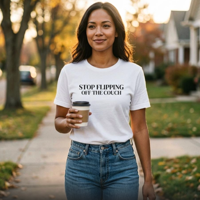 Woman wearing white “Stop Flipping Off the Couch” t-shirt walking outdoors holding coffee, everyday lifestyle look