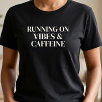 Close-up of black “Running on Vibes & Caffeine” graphic t-shirt showing bold typography and print detail