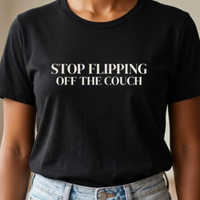 Close-up of black “Stop Flipping Off the Couch” graphic t-shirt with bold white typography