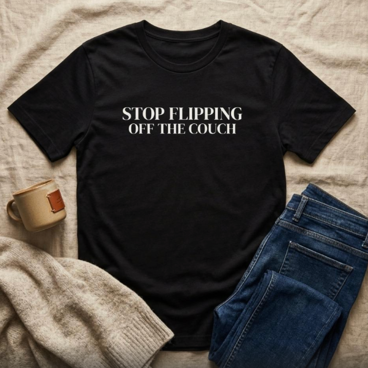 Black “Stop Flipping Off the Couch” graphic t-shirt flat lay styled with jeans and neutral accessories