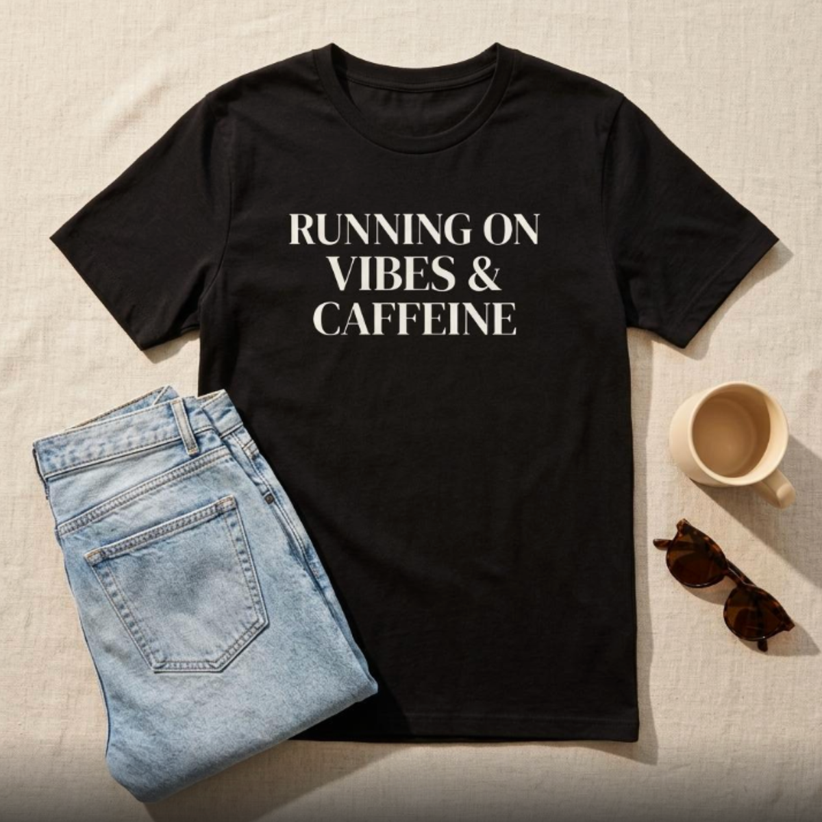 Black “Running on Vibes & Caffeine” graphic t-shirt flat lay with jeans and coffee, casual outfit styling