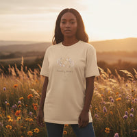 Woman wearing ivory Pisces Mama zodiac graphic t-shirt outdoors at sunset in a wildflower field