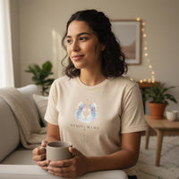 Latina woman holding mug wearing ivory Gemini Mama zodiac t-shirt in cozy indoor setting