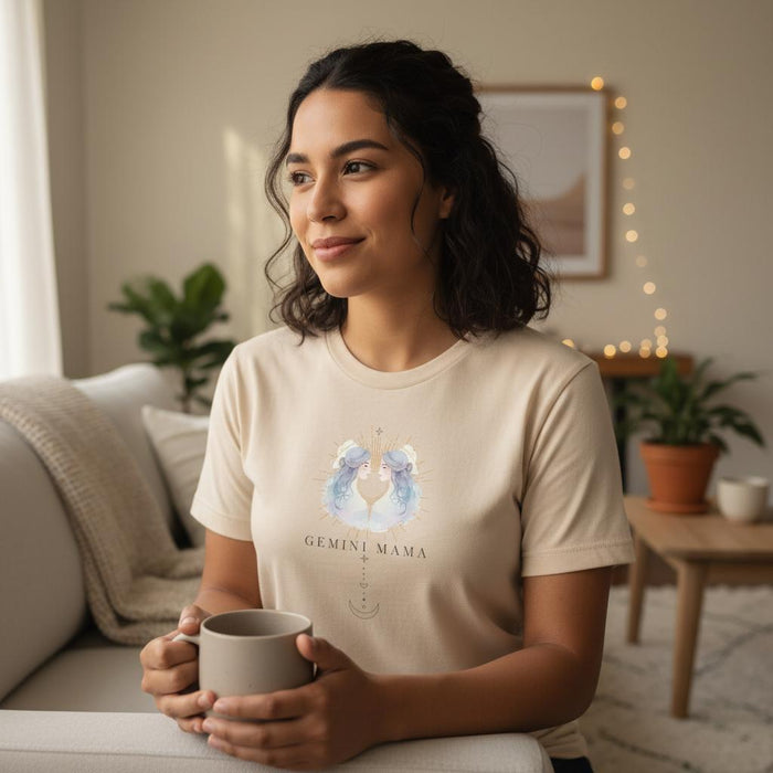 Latina woman holding mug wearing ivory Gemini Mama zodiac t-shirt in cozy indoor setting