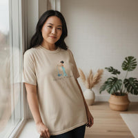 Asian woman modeling ivory Aquarius Mama zodiac t-shirt by a window with soft natural light and neutral home decor