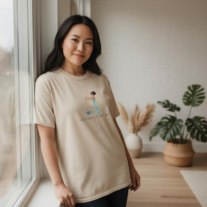 Asian woman modeling ivory Aquarius Mama zodiac t-shirt by a window with soft natural light and neutral home decor