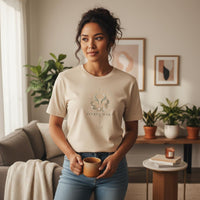 Woman wearing Taurus Mama ivory celestial graphic tee indoors holding coffee in cozy neutral living room