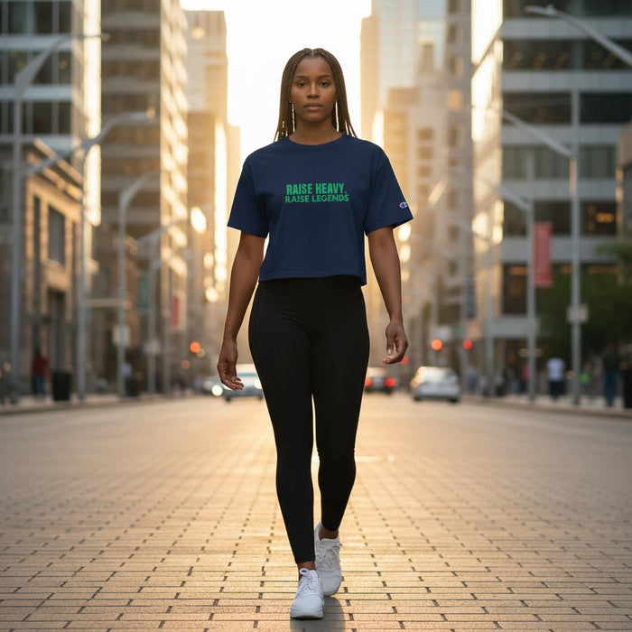 Woman walking confidently in a city wearing a navy cropped “Raise Heavy. Raise Legends.” Champion t-shirt and black leggings
