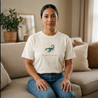 Latina woman wearing Scorpio Mama ivory zodiac graphic t-shirt seated indoors on neutral sofa
