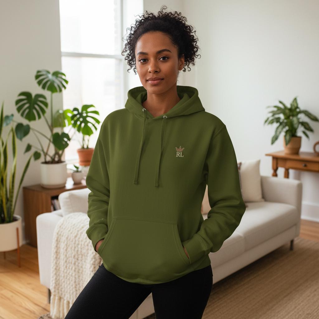 Woman wearing an olive green Raising Legends hoodie with small crown logo on the front, styled in a bright, modern living room.