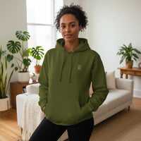 Woman wearing an olive green Raising Legends hoodie with small crown logo on the front, styled in a bright, modern living room.