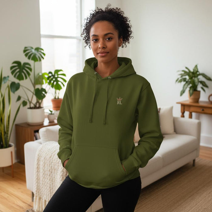 Woman wearing an olive green Raising Legends hoodie with small crown logo on the front, styled in a bright, modern living room.