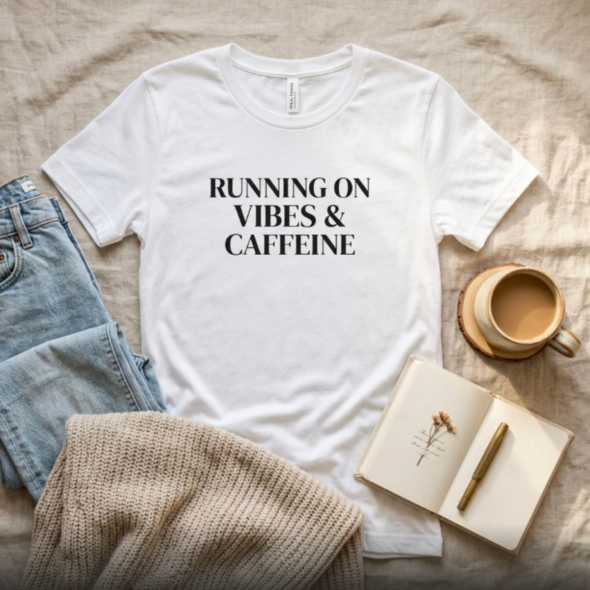 White “Running on Vibes & Caffeine” graphic t-shirt flat lay with jeans and coffee, neutral styled outfit