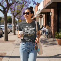 Asian woman wearing Pepper “I Can’t My Kid Has Practice” shirt tucked into jeans, walking on a sunny sidewalk holding coffee and tote bag.