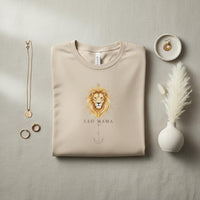 Flat lay of ivory Leo Mama zodiac graphic t-shirt folded with neutral jewelry and decor accents