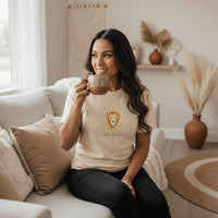 Latina woman sitting indoors wearing an ivory Leo Mama zodiac graphic t-shirt and jeans