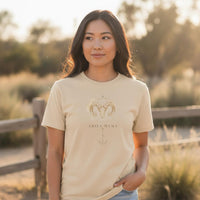 Woman wearing ivory Aries Mama zodiac t-shirt with watercolor ram design outdoors in natural sunlight