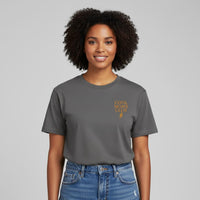 Smiling woman wearing a Comfort Colors t-shirt in Pepper with 'Cool Moms Club' text and a neutral background.