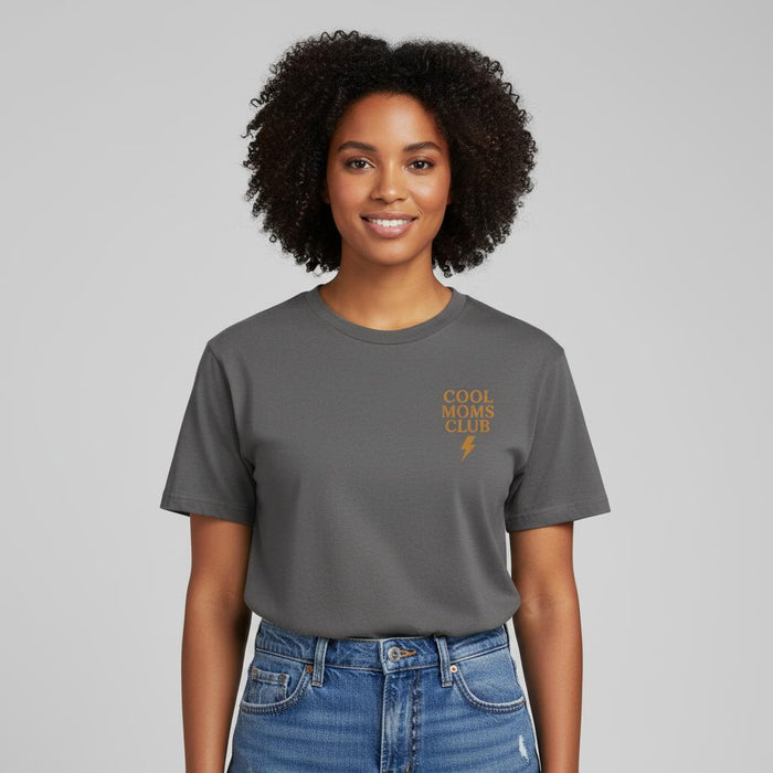 Smiling woman wearing a Comfort Colors t-shirt in Pepper with 'Cool Moms Club' text and a neutral background.