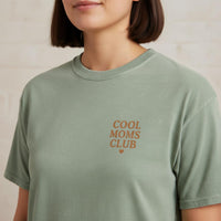Woman wearing a green t-shirt with 'Cool Moms Club' text on a neutral background